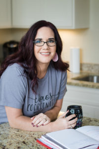 picture of teresa stone leaning on a kitchen counter holding a coffee cup with a planner on the counter in front of her